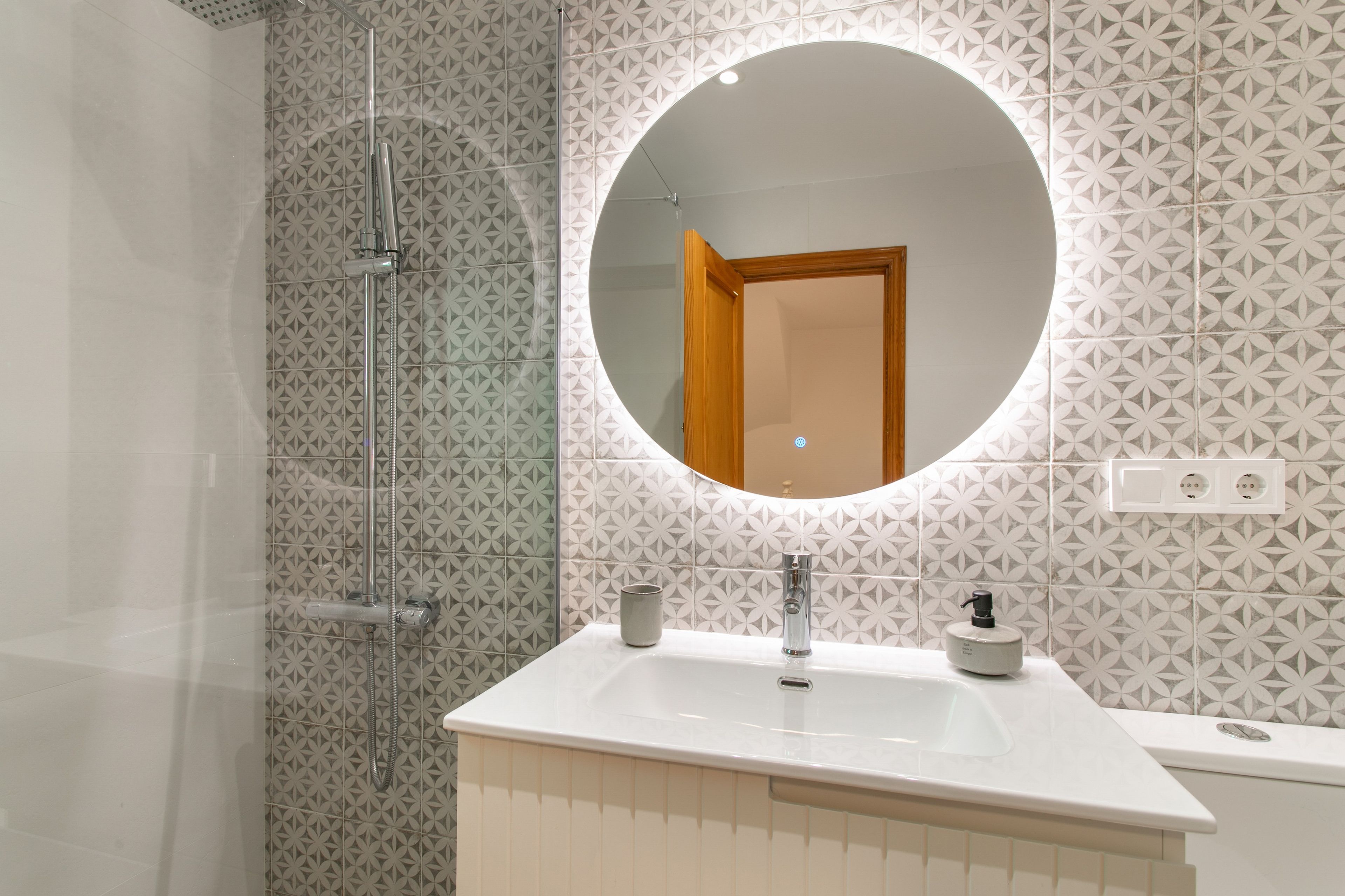 Een badkamer met een glazen douchecabine, een ronde spiegel en een witte wastafel met een kraan.