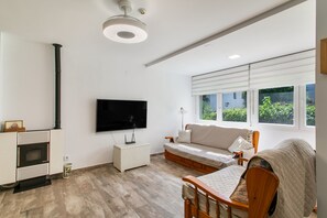 A modern living room with a flat-screen TV, a sofa, a wooden chair, and a fireplace. - Holiday Home 'Sun, Beach, Pools & Gardens' with Shared Pool, Wi-Fi & Air Conditioning (Gran Alacant)
