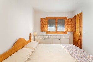 A bedroom with a bed, a nightstand, a dresser, and a window with wooden shutters. - Holiday Home 'Sun, Beach, Pools & Gardens' with Shared Pool, Wi-Fi & Air Conditioning (Gran Alacant)