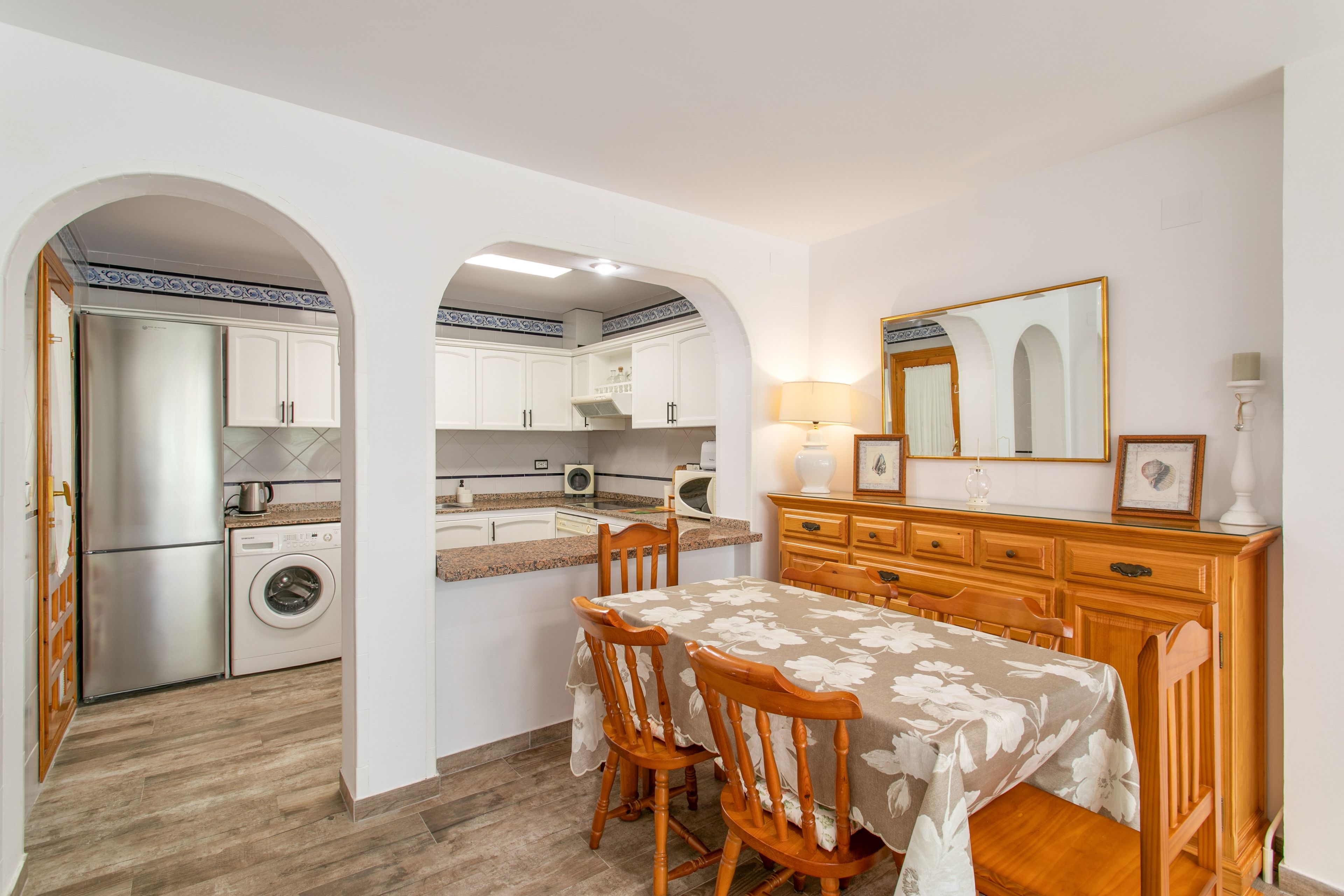 Une cuisine compacte avec des meubles blancs, un lave-linge encastré et un coin repas comprenant une table et des chaises.