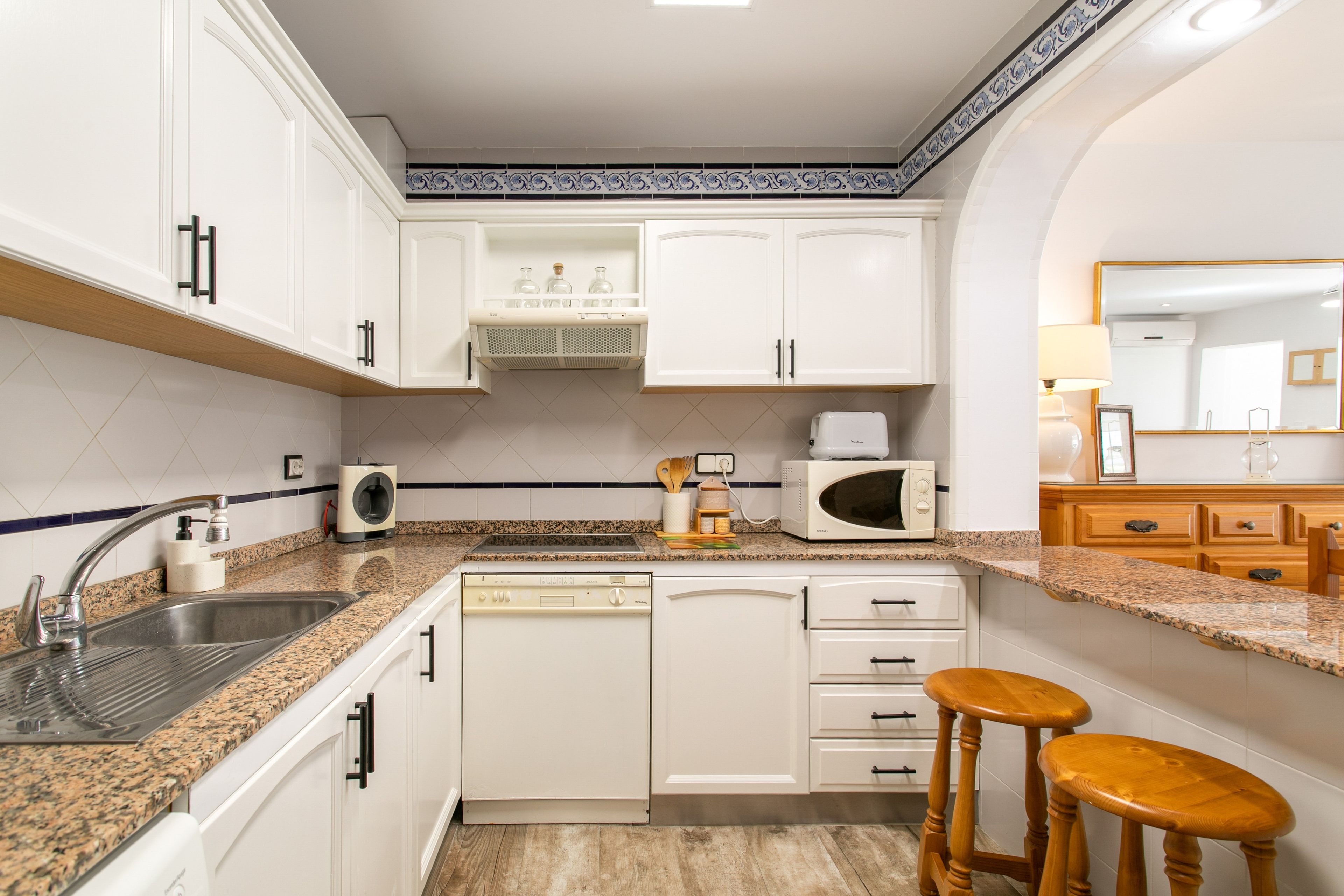 A compact kitchen with white cabinets, a granite countertop, a built-in dishwasher, and a microwave.