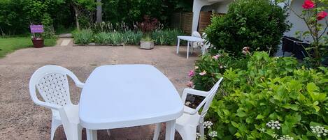Une terrasse avec une table et des chaises blanches, entourée de verdure et donnant sur un immeuble doté d’un balcon.