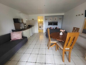 A modern living room with a sofa, a dining table with chairs, a kitchen area, and a bathroom visible through an open doorway.