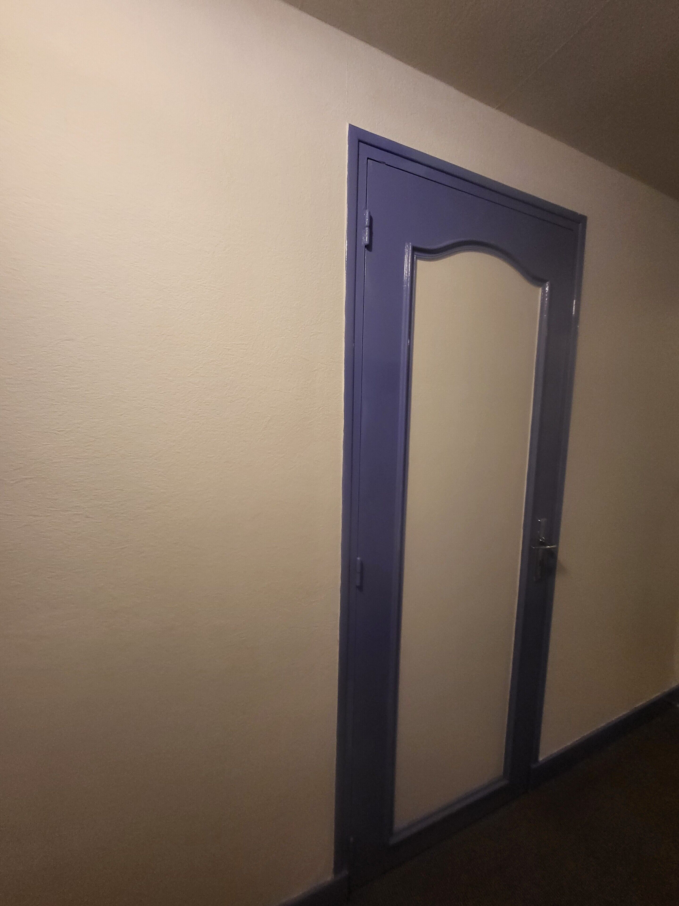 Een gang met een gesloten deur en een lichtschakelaar aan de muur.