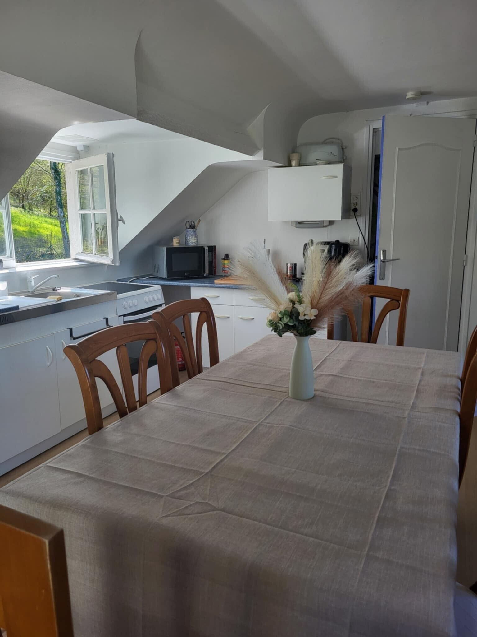 Een eetgedeelte met een tafel voor vier personen, een bloevas en een keuken op de achtergrond.