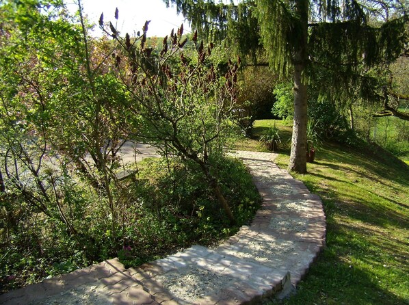A paved garden path with a brick border, surrounded by lush greenery and trees.