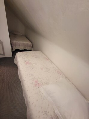Ett litet, svagt upplyst rum med två enkelsängar, varav den ena har ett blommigt sängöverkast och den andra ett enfärgat.