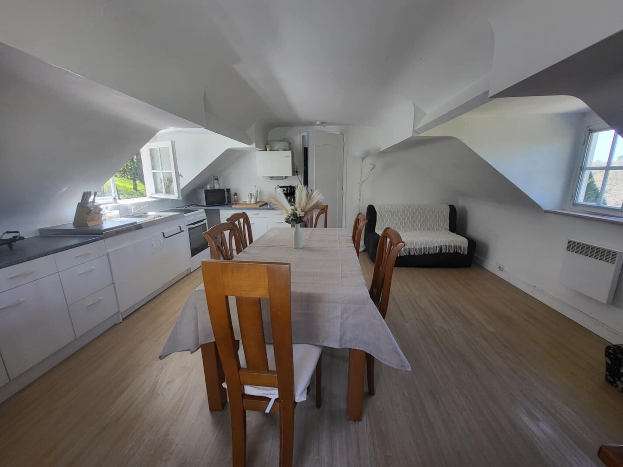 Eine kompakte Küche mit weißen Schränken, einem Esstisch mit Stühlen und einer Couch.