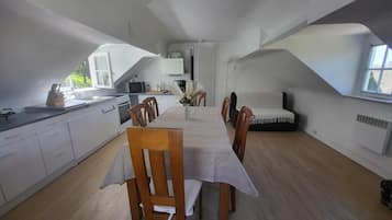 Eine kompakte Küche mit weißen Schränken, einem Esstisch mit Stühlen und einer Couch.