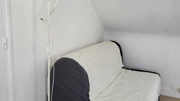 Ein kleines Zimmer mit einem Einzelbett, einer weißen Stehlampe und einem dunkelgrauen Sofa.