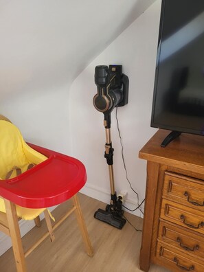 Ett rum med ett skrivbord i trä, en tv, en röd och gul barnstol och en kamera som är monterad på ett stativ.