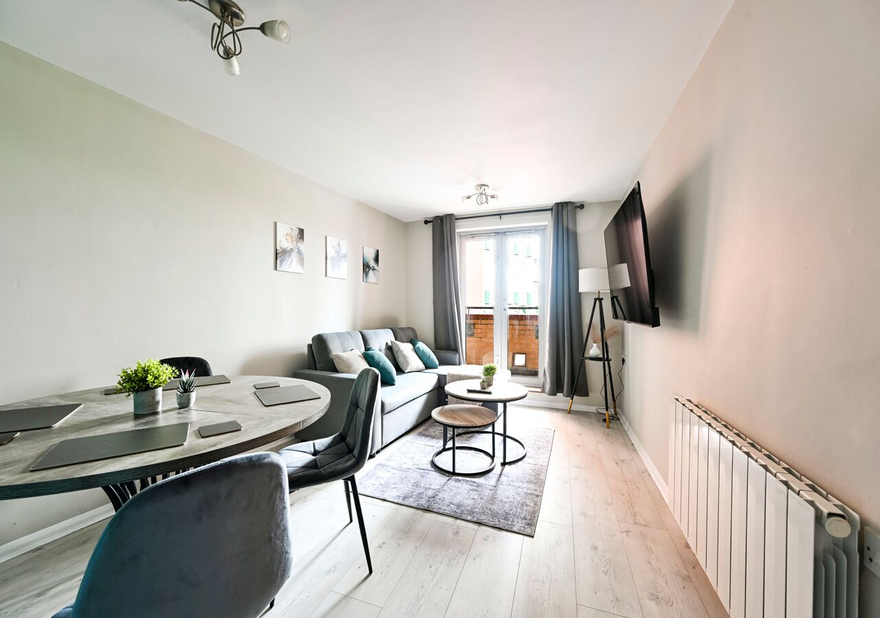 A modern living room with a sofa, a dining table with chairs, a small coffee table, and a TV mounted on the wall.