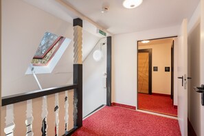 A hotel corridor with a red carpet, a staircase with a unique railing design, and a door with a number plate. - Apartment "London Single Room" with Shared Garden and Wi-Fi (Weißenfels)