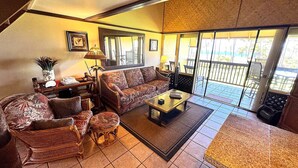 A living room with a sofa, armchairs, a coffee table, and a dining table. There is a balcony with a view.