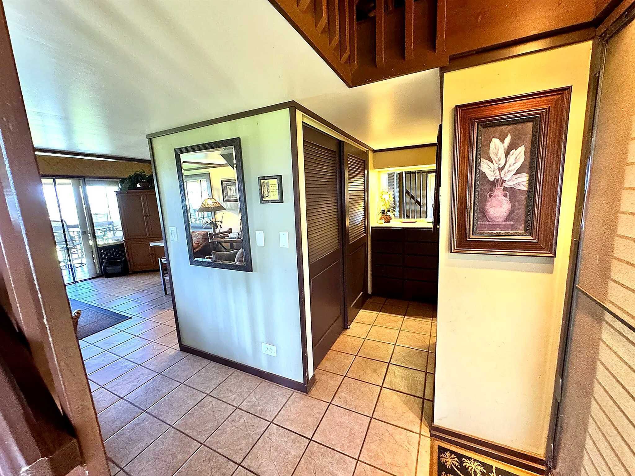 A hallway with a tiled floor, a door with a mirror, and framed artwork on the walls.