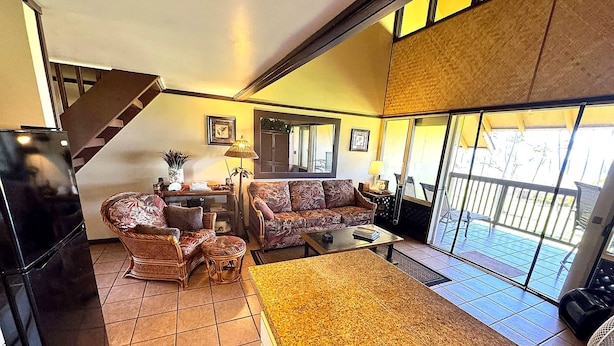 A living room with a sofa, chairs, a coffee table, and a rug. There is a staircase leading to an upper level.