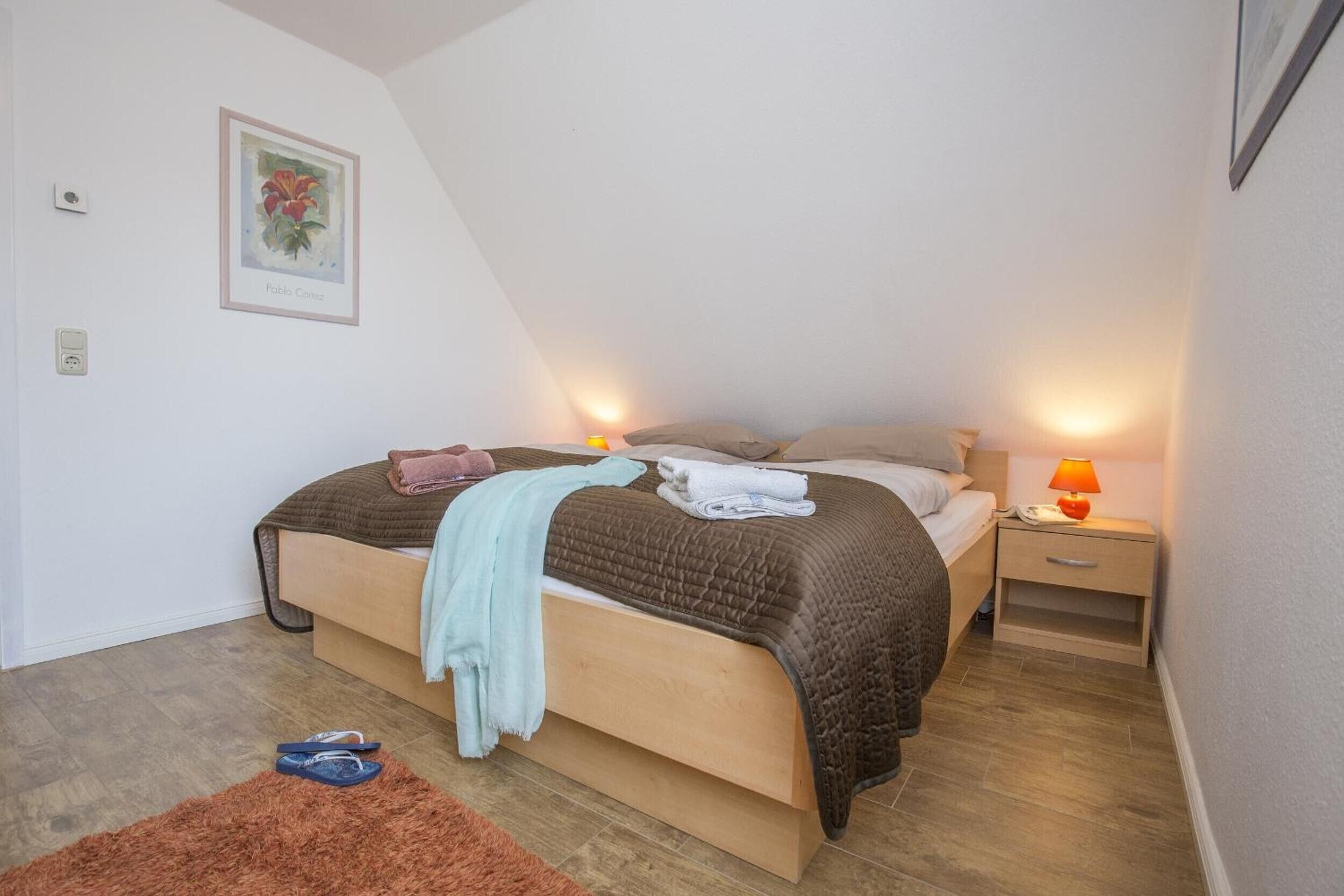 Une chambre à coucher avec un lit, des tables de chevet, une lampe et un tableau encadré au mur.