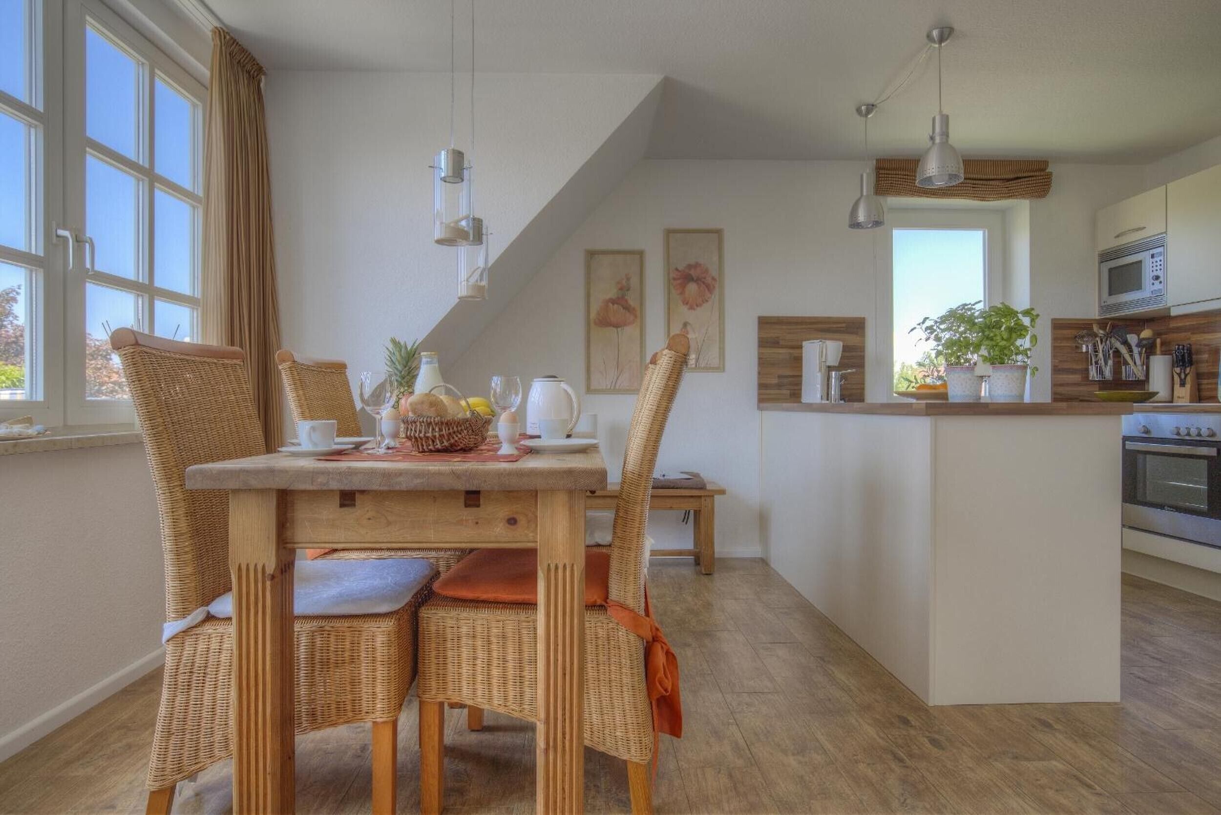 A dining area with wicker chairs, a wooden table, and a kitchen in the background.