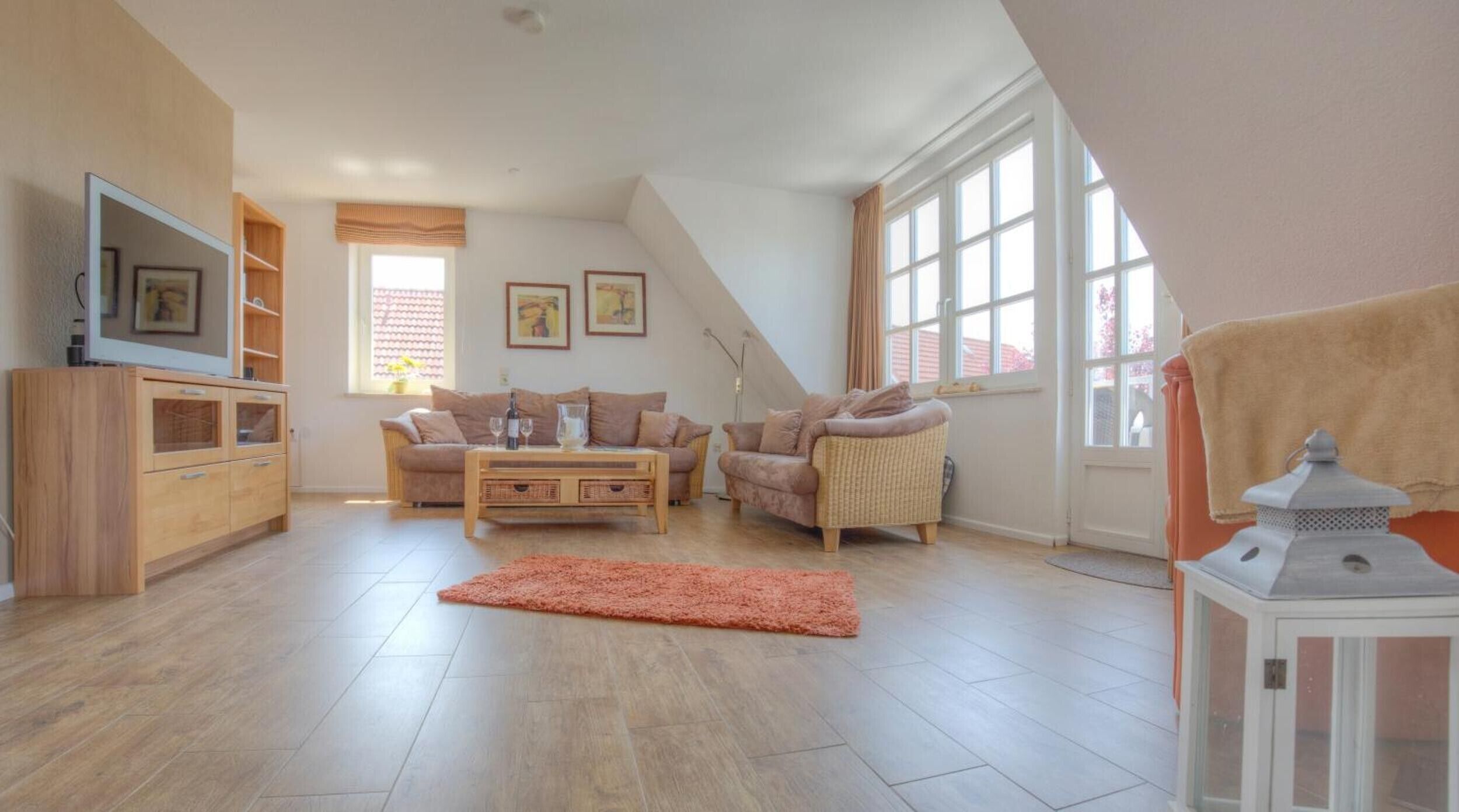 Un salon spacieux avec un plafond haut, un téléviseur fixé au mur, un ensemble de canapés, une table basse et un tapis décoratif.
