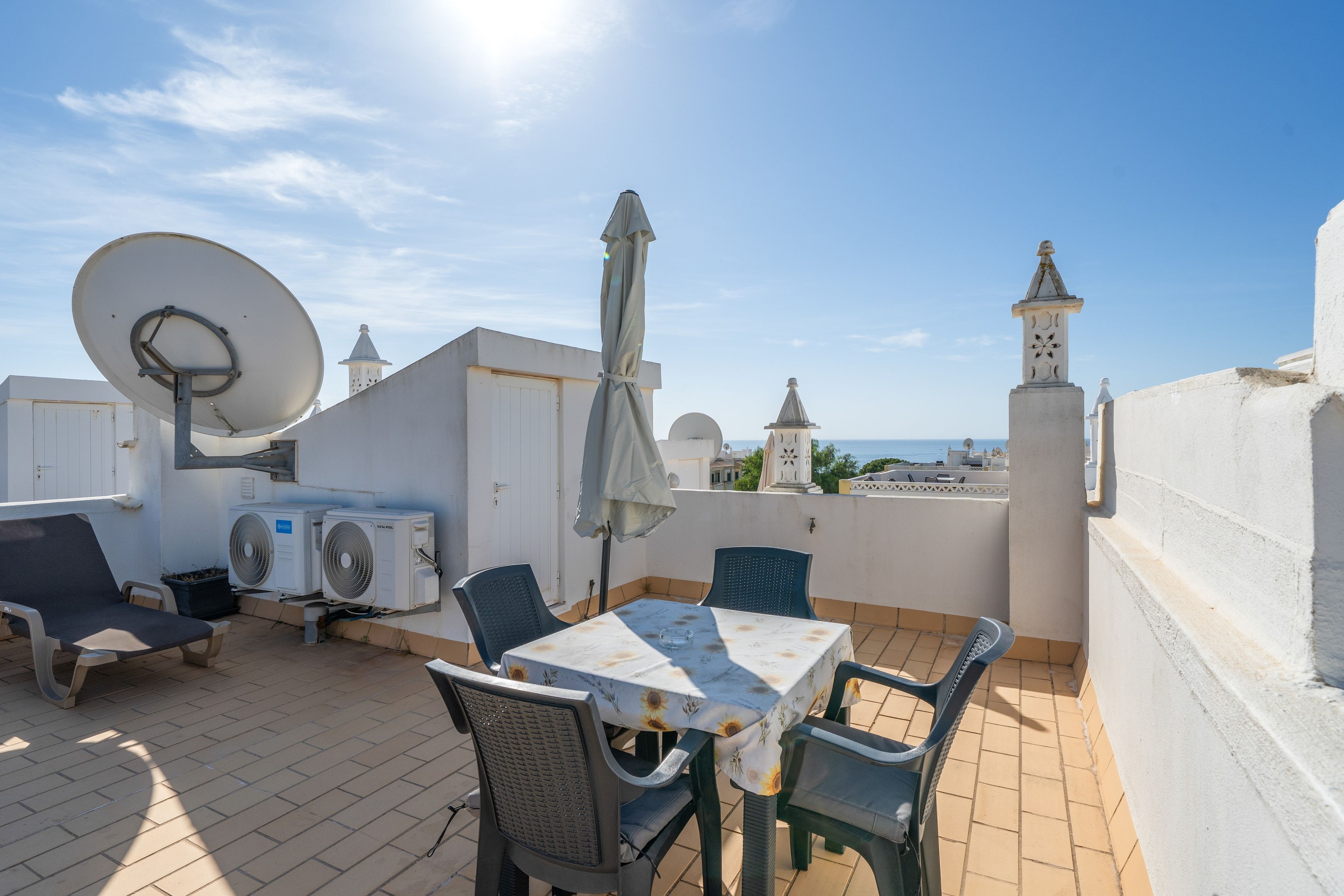 A rooftop terrace with a table, chairs, a satellite dish, and a view of the sea.