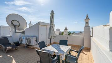 A rooftop terrace with a table, chairs, a satellite dish, and a view of the sea.
