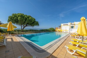 Ein Swimmingpool mit Liegestühlen und Sonnenschirmen, umgeben von einem Zaun und einem Baum.