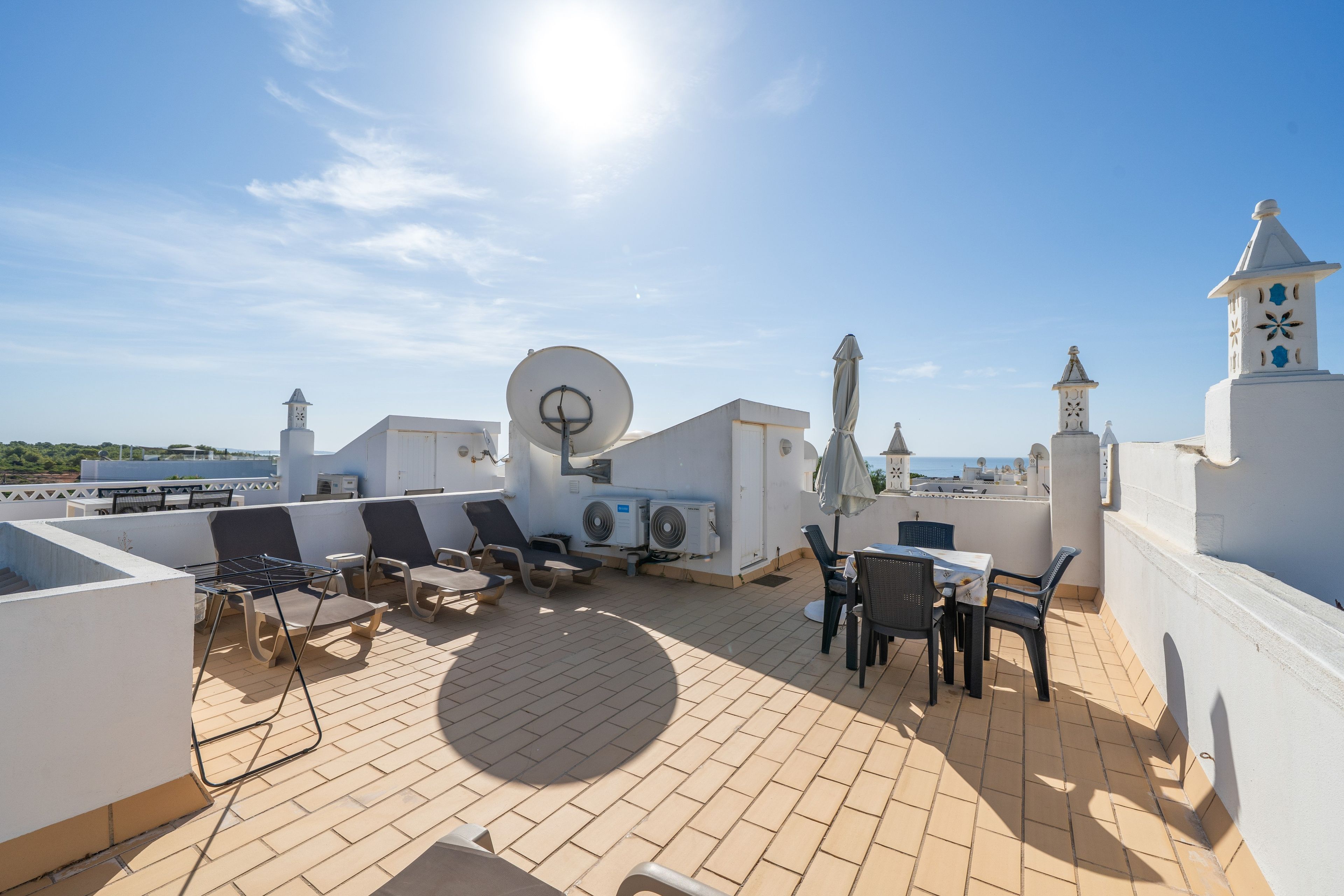 A rooftop terrace with lounge chairs, a table, and a view of the sea.