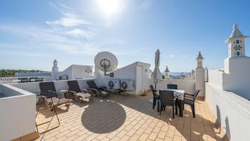 A rooftop terrace with lounge chairs, a table, and a view of the sea.