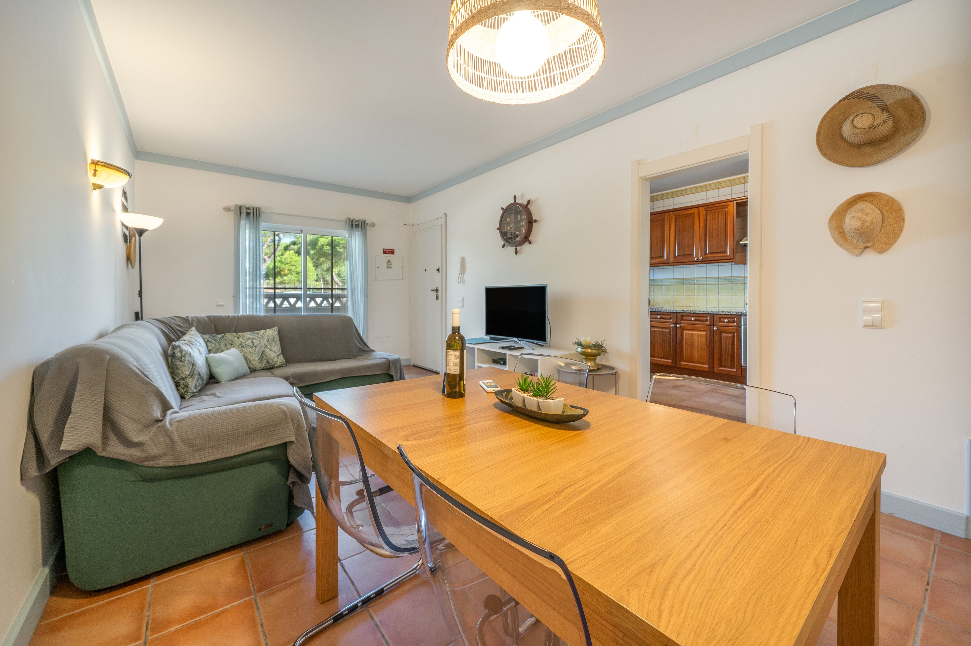 A modern living space with a dining area, a sofa, a television, and a kitchen visible through an open door.