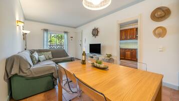 A modern living space with a dining area, a sofa, a television, and a kitchen visible through an open door.