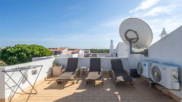 A rooftop terrace with lounge chairs, a satellite dish, and an air conditioning unit.