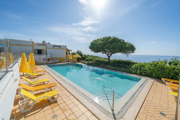 A swimming pool with yellow sun loungers and a tree in the background.