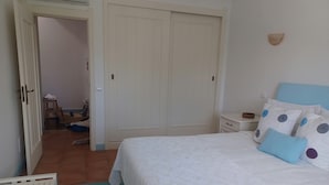 Un dormitorio con cama, mesita de noche, armario y baño visible a través de una puerta abierta.