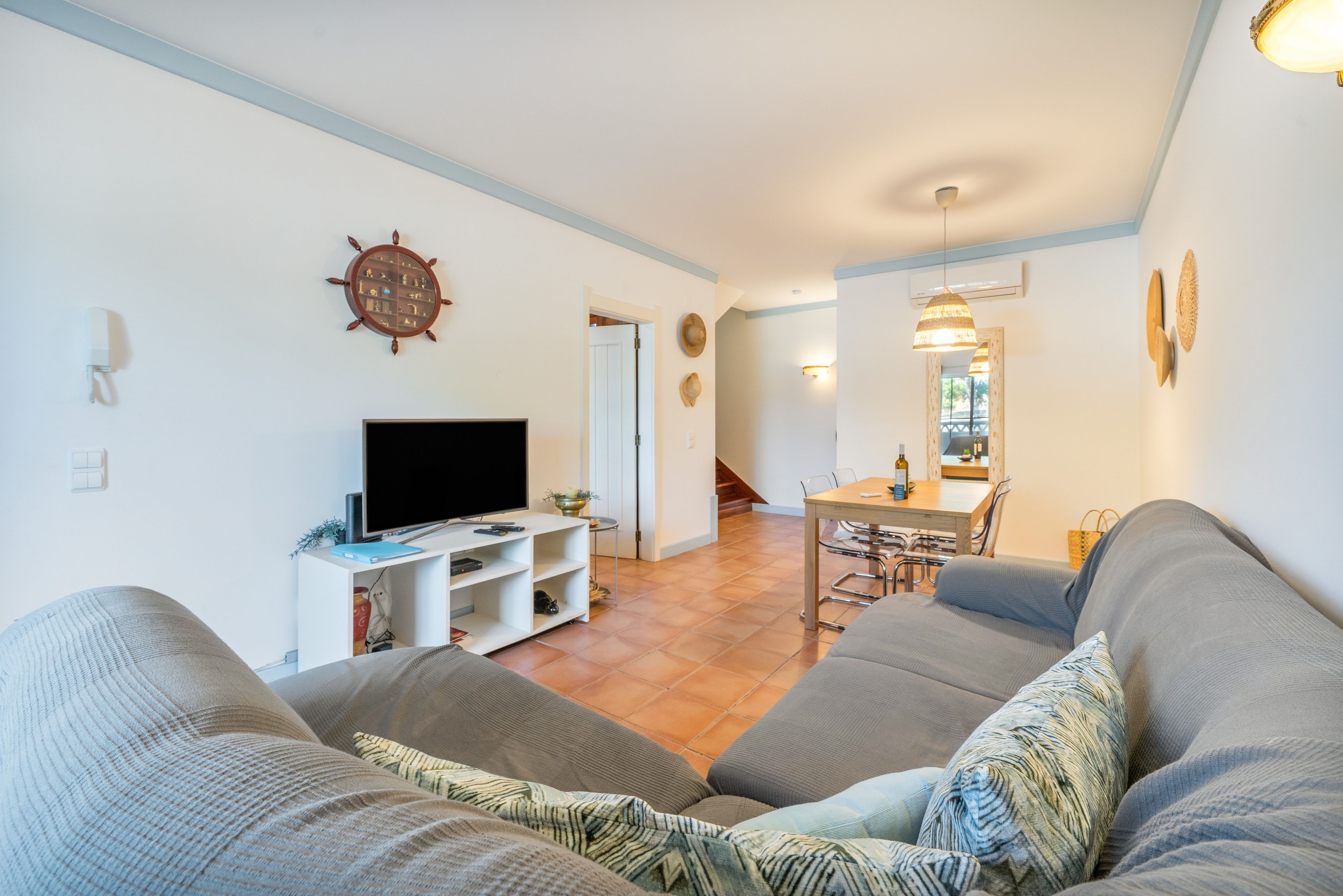 A living room with a television, a dining area with a table and chairs, and a staircase leading to another level.