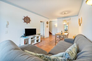 A living room with a television, a dining area with a table and chairs, and a staircase leading to another level.