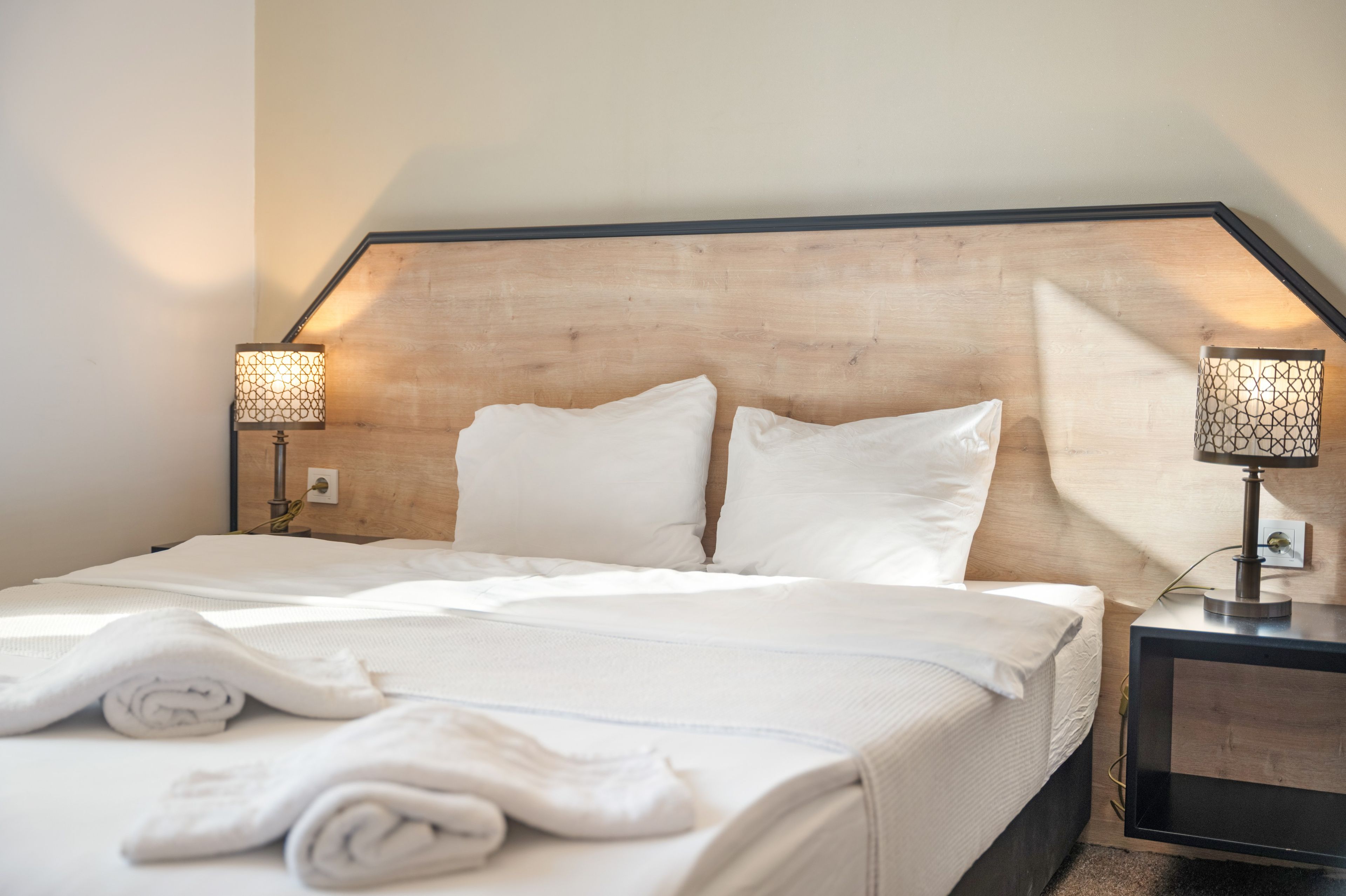 A neatly made bed with white linens and pillows, two bedside lamps with patterned shades, and a wooden headboard.