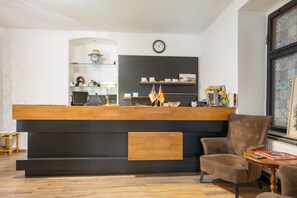 Un mostrador de recepción con un reloj encima, una estantería con objetos decorativos y una silla en primer plano.