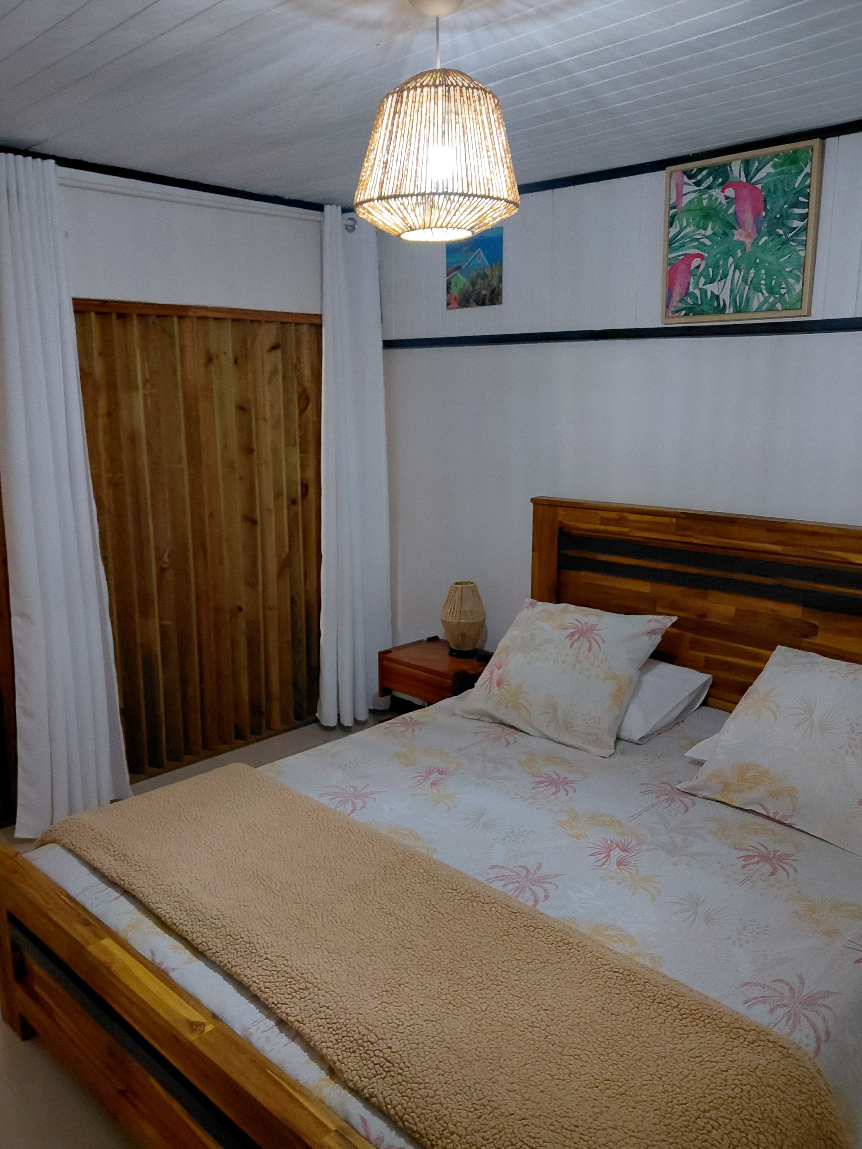 Un dormitorio con una cama de madera, una mesita de noche, una lámpara colgante y un cuadro en la pared.