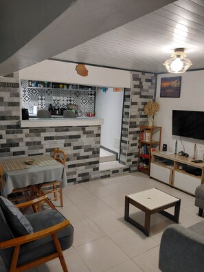 Una sala de estar moderna con comedor, televisor y cocina al fondo.