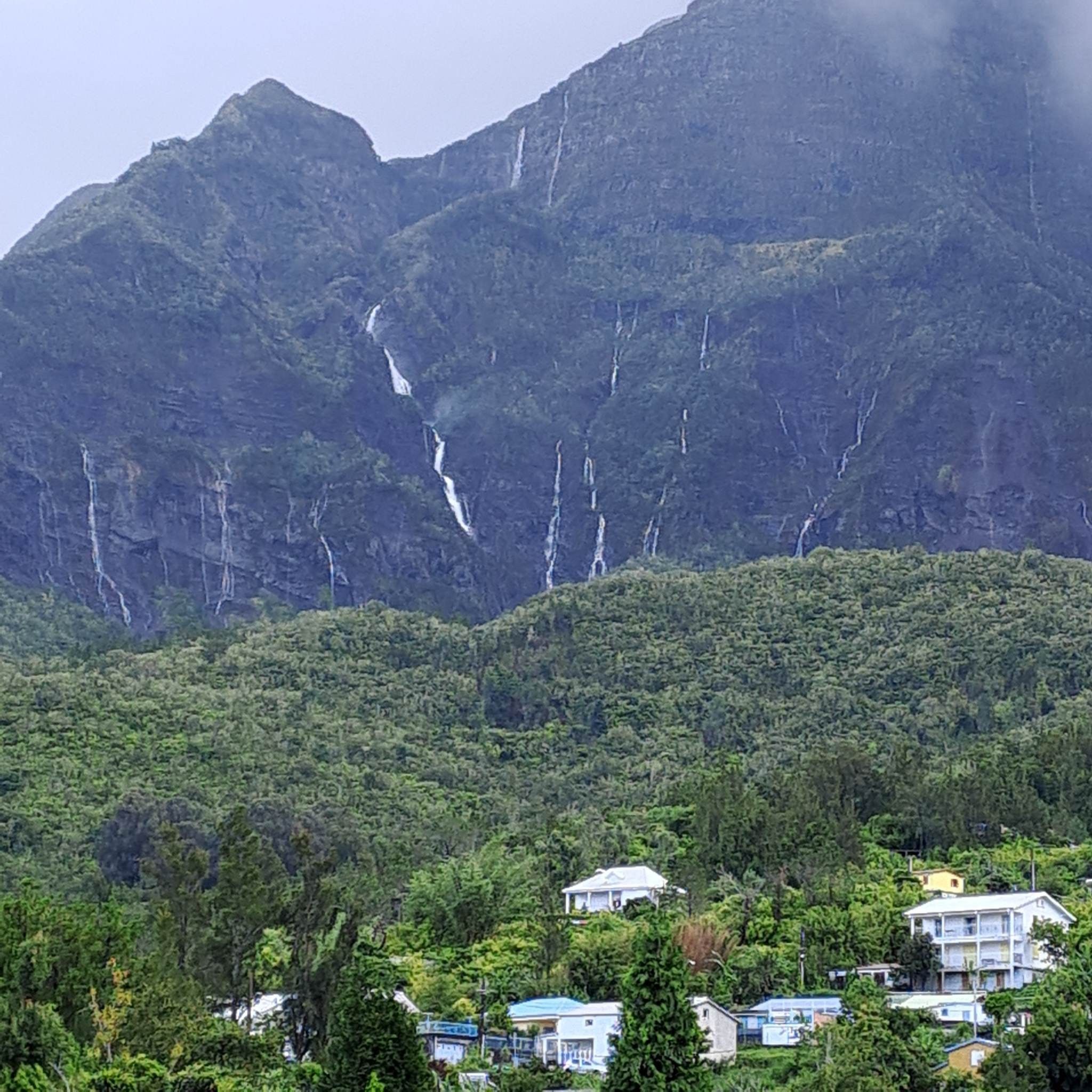 Un paysage montagneux avec une cascade et des immeubles d’habitation au premier plan.