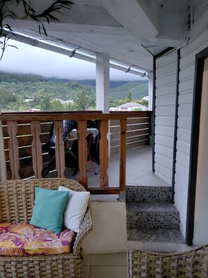 Un balcon avec un canapé en osier et une petite table, offrant une vue sur un paysage montagneux.