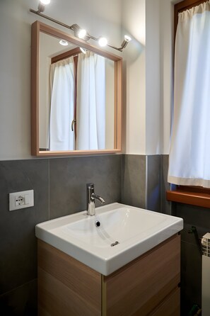 A bathroom with a white sink, a mirror, and a window with a curtain. - ‘Dolomis Margherita 4px’ Apartment with Mountain View, Shared Garden and Wi-Fi (Caderzone Terme)