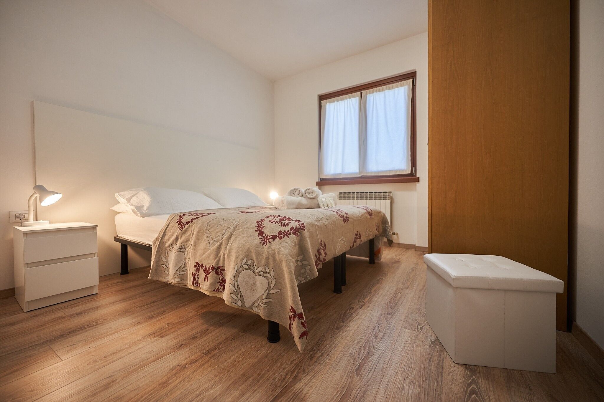 A bedroom with a bed, bedside tables, a nightstand, a window, and a radiator.