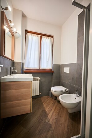 A modern bathroom with a wooden vanity, a bidet, a toilet, and a window with curtains. - ‘Dolomis Margherita 4px’ Apartment with Mountain View, Shared Garden and Wi-Fi (Caderzone Terme)