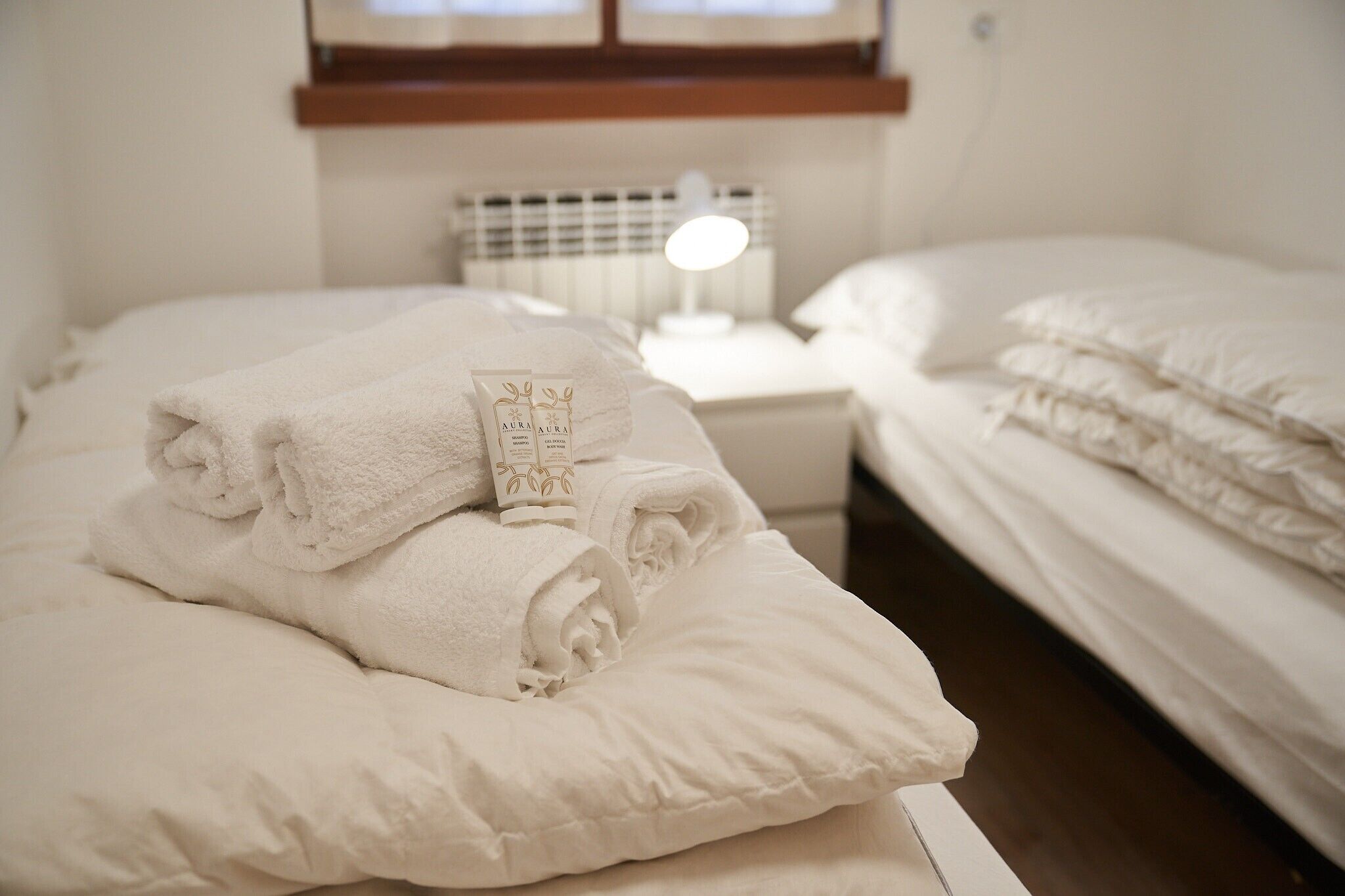 A neatly made bed with folded white towels and a tube of lotion on the nightstand.