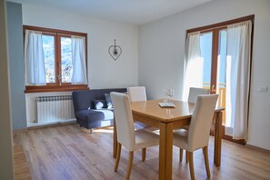 A dining area with a wooden table and four chairs, a sofa, and a radiator. - ‘Dolomis Margherita 4px’ Apartment with Mountain View, Shared Garden and Wi-Fi (Caderzone Terme)