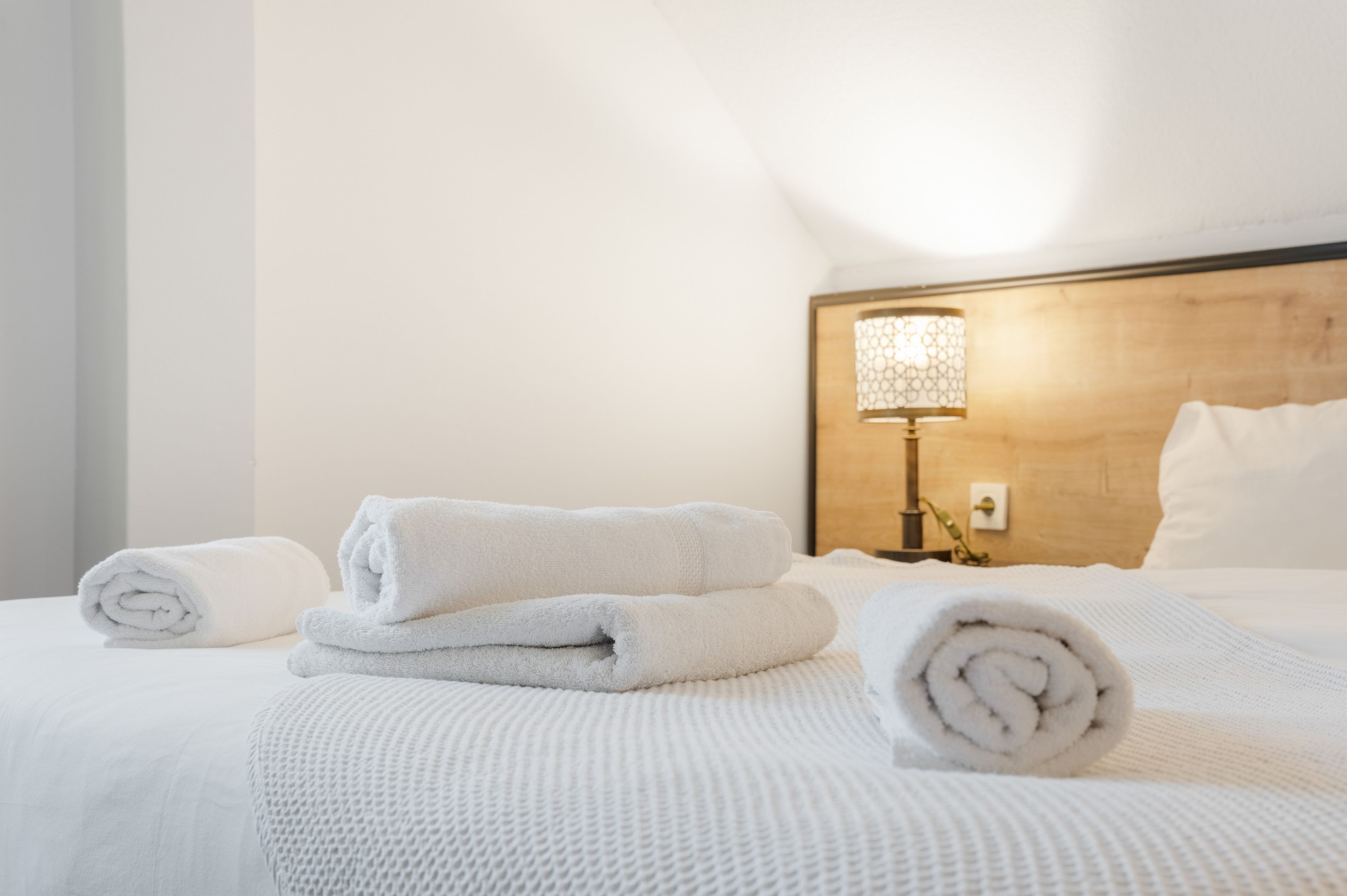 A neatly made bed with rolled white towels and a headboard with a light fixture.