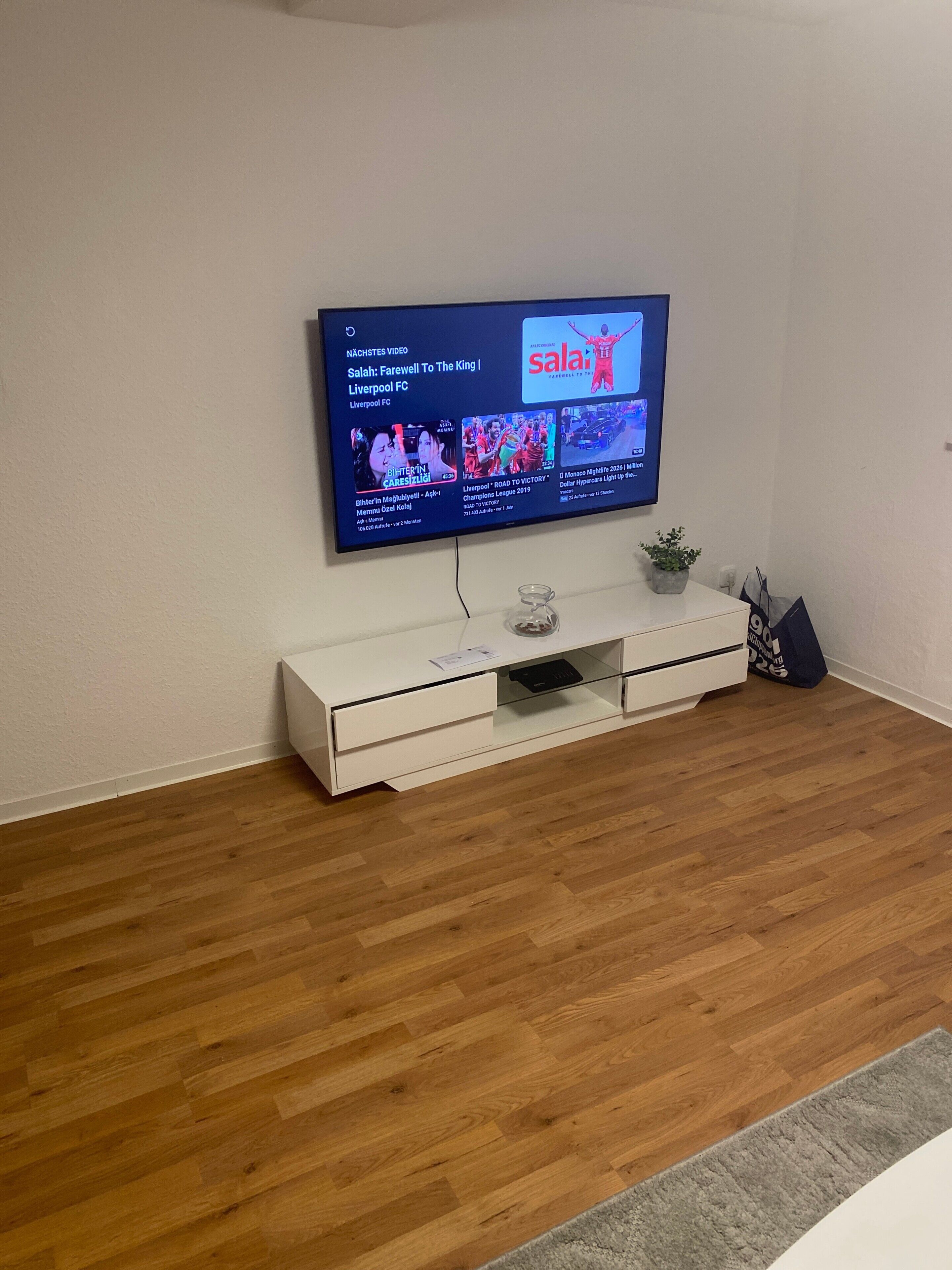A flat-screen TV mounted on a white wall, a white entertainment unit below it, and a wooden floor.