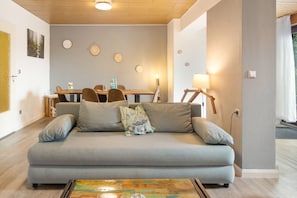 A living room with a grey sofa, a coffee table with a painting, a dining area with a table and chairs, and a wall with circular decorations.