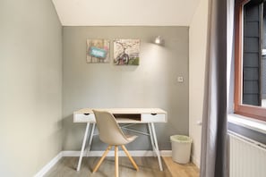 A corner room with a desk, chair, and artwork on the wall.